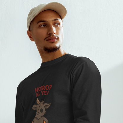 This is a man with a baseball hat wearing a black long sleeve shirt with a cartoon illustration of a baby Baphomet goat with curved horns and a playful grin, wearing bright floral swim trunks while floating in a colorful inner tube. The character is set against a light background with the bold text “Horror All Year” above in red letters
