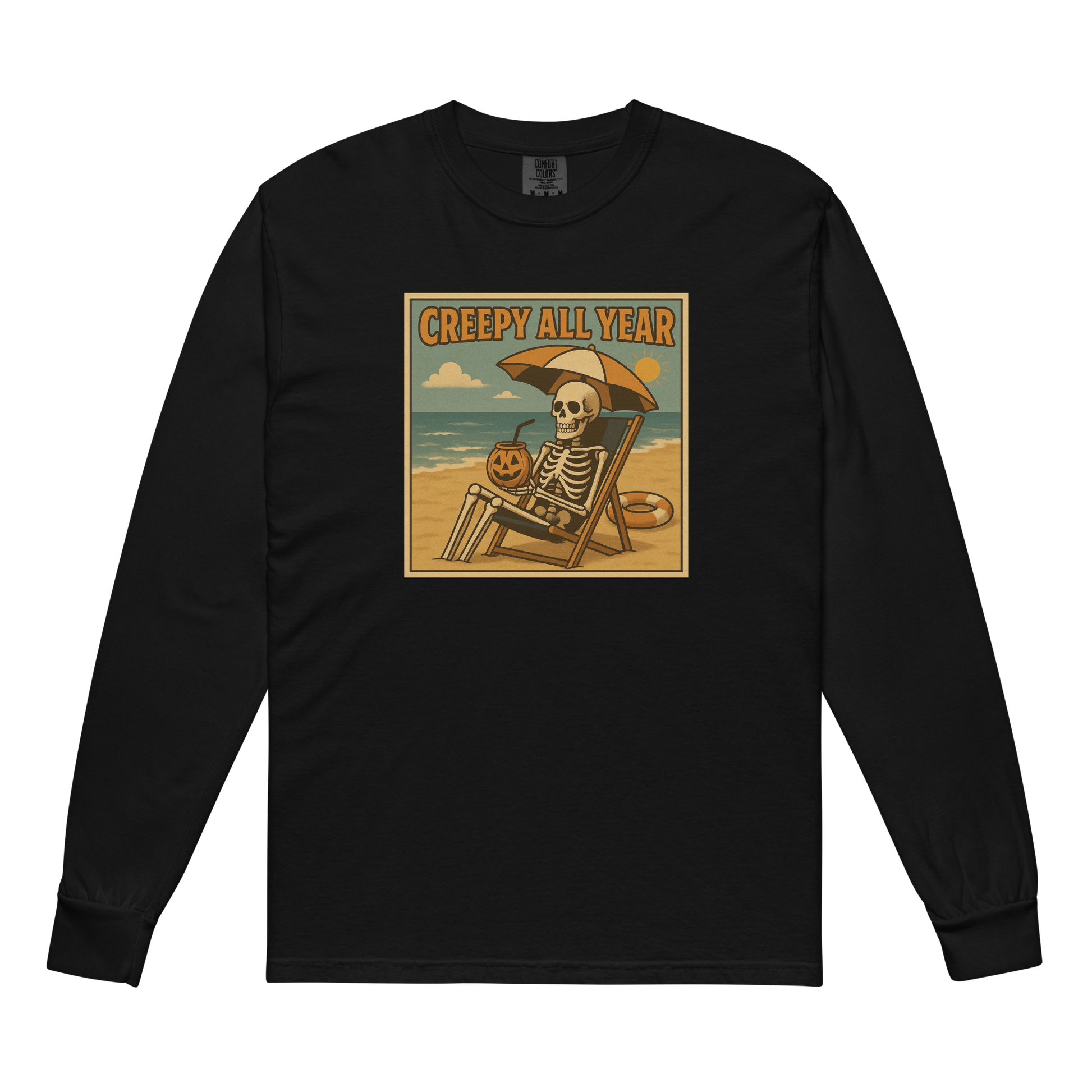 This is a black long-sleeve shirt with a retro-style illustration of a grinning skeleton lounging on a beach chair under an orange umbrella. The skeleton is holding a pumpkin-shaped drink cup with a straw and relaxing by the ocean, with a bright sun in the sky and a life preserver in the sand. The words “Creepy All Year” appear boldly at the top