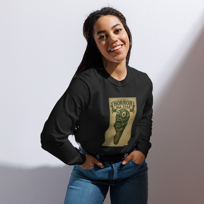 This is a woman with black braids wearing a black long sleeve shirt that is a vintage-style illustration of a zombie-themed ice cream cone with a green, melting undead face and bulging eyeballs. Above the cone, a horror banner reads "Horror All Year" on a distressed parchment background