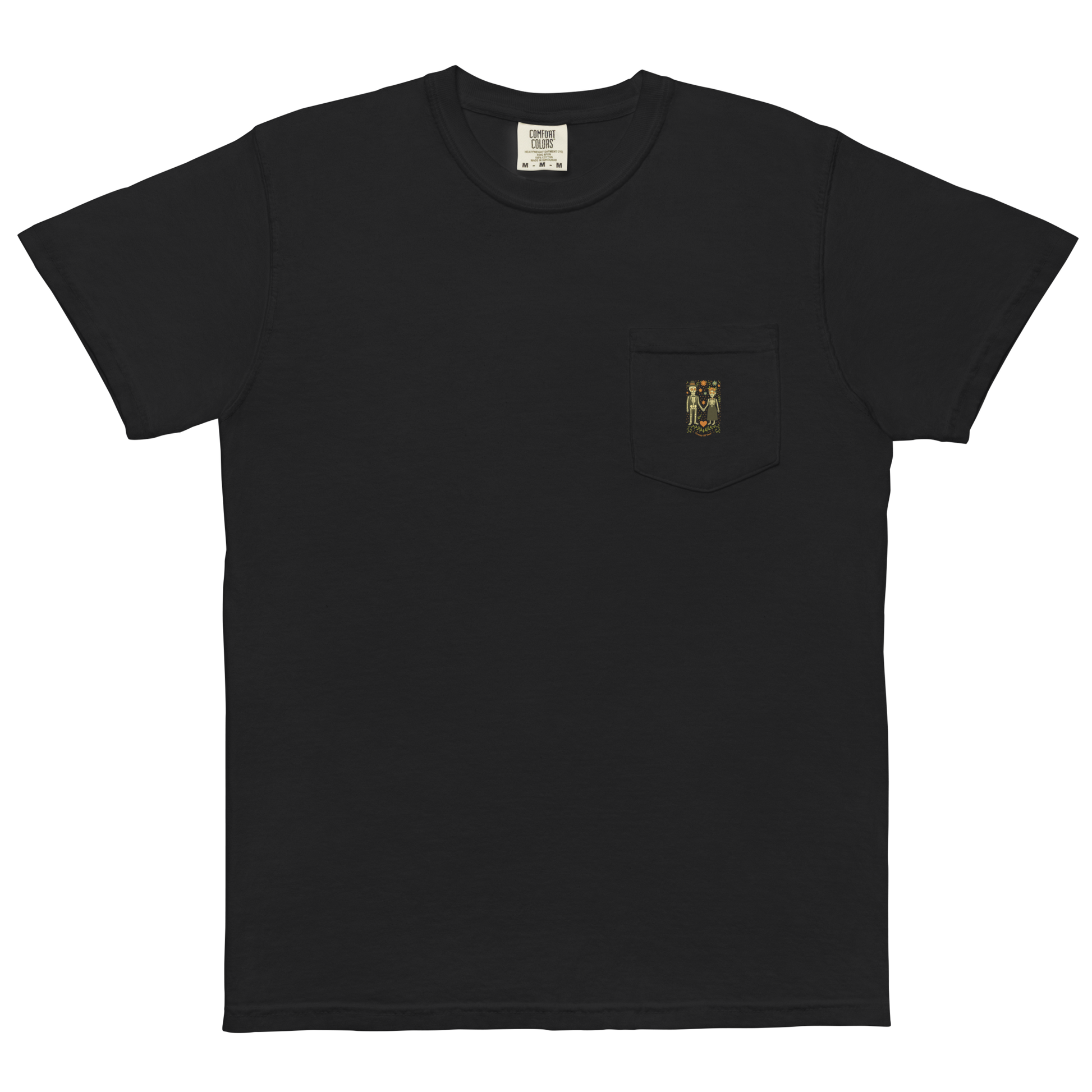 This is a black pocket t-shirt with a Día de los Muertos–style illustration of a male and female skeleton holding hands, surrounded by marigolds, vines, and folk art patterns. The skeletons wear traditional black clothing, the man in a suit and hat, the woman with a floral crown with a red heart and leaves at the bottom and the text Creepy All Year. Rendered in warm tones of orange, green, and cream, symbolizing eternal love and remembrance