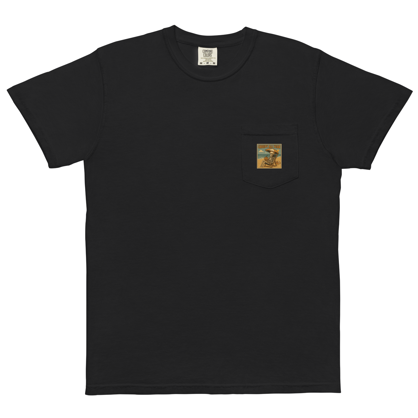 This is a black pocket t-shirt with a retro-style illustration of a grinning skeleton lounging on a beach chair under an orange umbrella. The skeleton is holding a pumpkin-shaped drink cup with a straw and relaxing by the ocean, with a bright sun in the sky and a life preserver in the sand. The words “Creepy All Year” appear boldly at the top