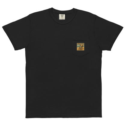 This is a black pocket t-shirt with a retro-style illustration of a grinning skeleton lounging on a beach chair under an orange umbrella. The skeleton is holding a pumpkin-shaped drink cup with a straw and relaxing by the ocean, with a bright sun in the sky and a life preserver in the sand. The words “Creepy All Year” appear boldly at the top