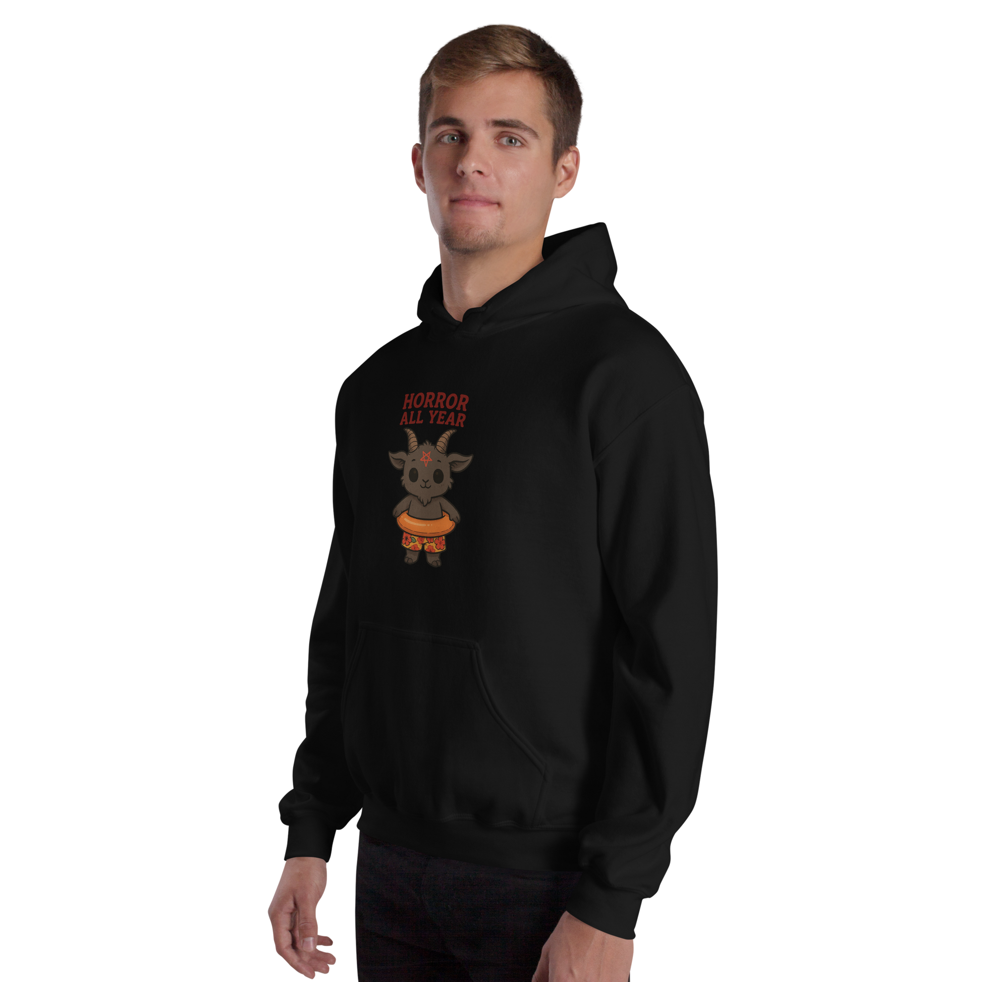 This is a man with light hair wearing a black hoodie with a cartoon illustration of a baby Baphomet goat with curved horns and a playful grin, wearing bright floral swim trunks while floating in a colorful inner tube. The character is set against a light background with the bold text “Horror All Year” above in red letters