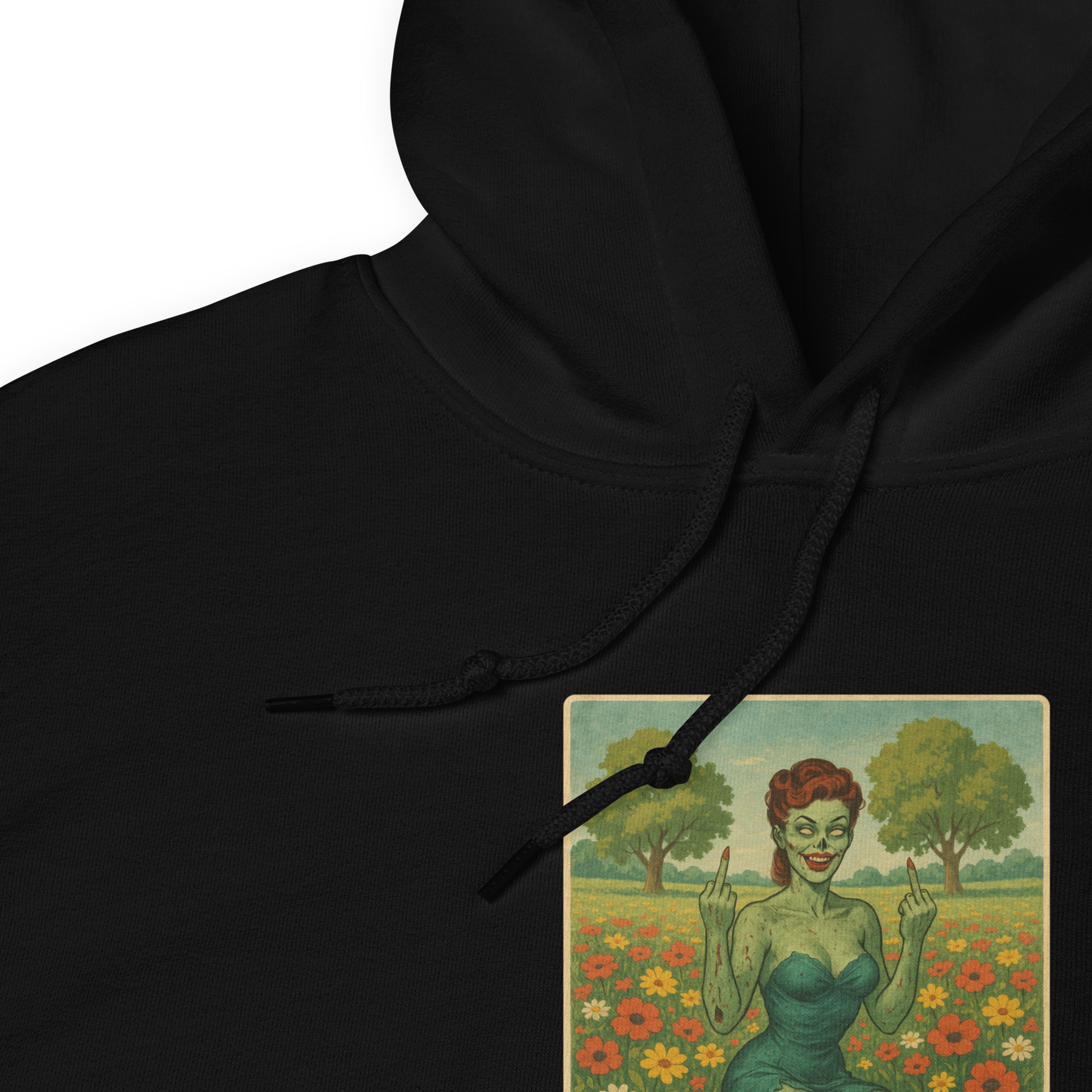 This is a zoom in of a black hoodie with a design illustration of a sassy zombie pinup girl standing in a floral field, wearing tattered lingerie and flipping off the viewer with both hands. She has green skin, vintage curls, and a bold attitude. The design blends horror and humor, with a pastel color palette and creepy cute vibes.