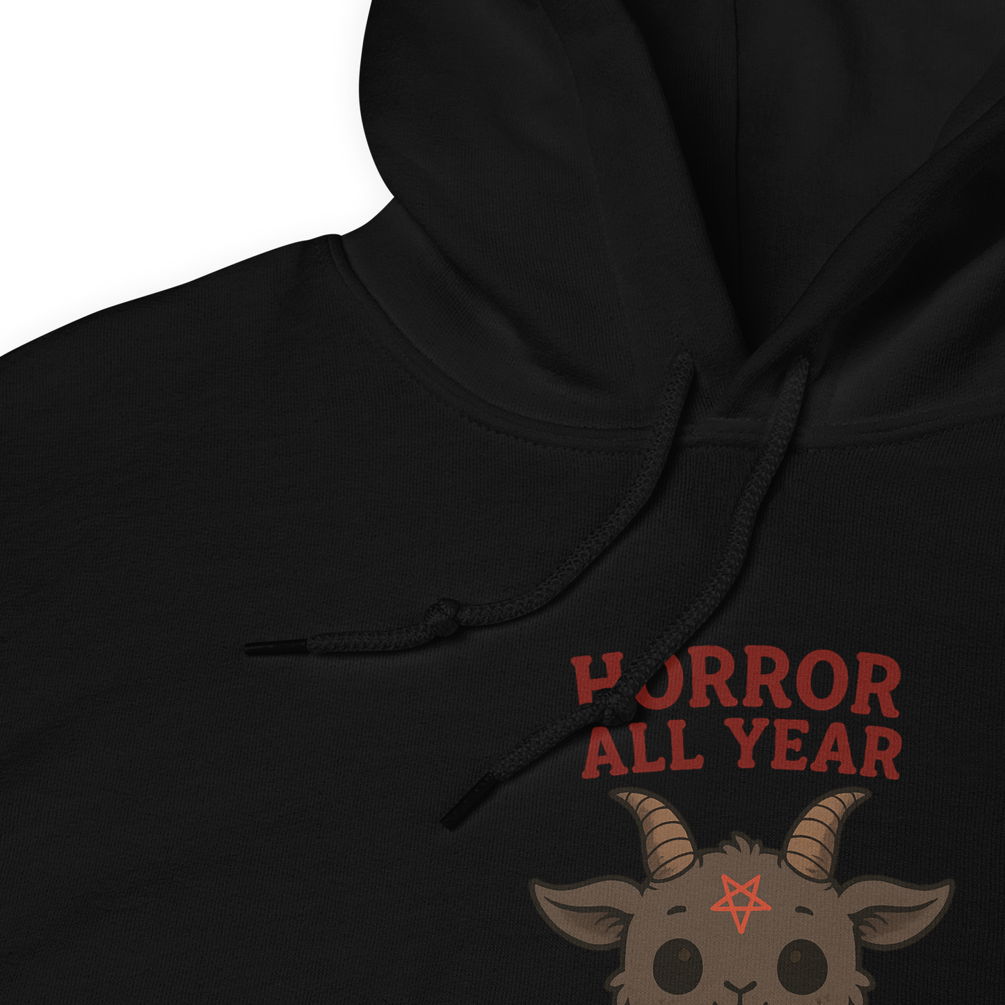 This is a zoom in of a black hoodie with cartoon illustration of a baby Baphomet goat with curved horns and a playful grin, wearing bright floral swim trunks while floating in a colorful inner tube. The character is set against a light background with the bold text “Horror All Year” above in red letters