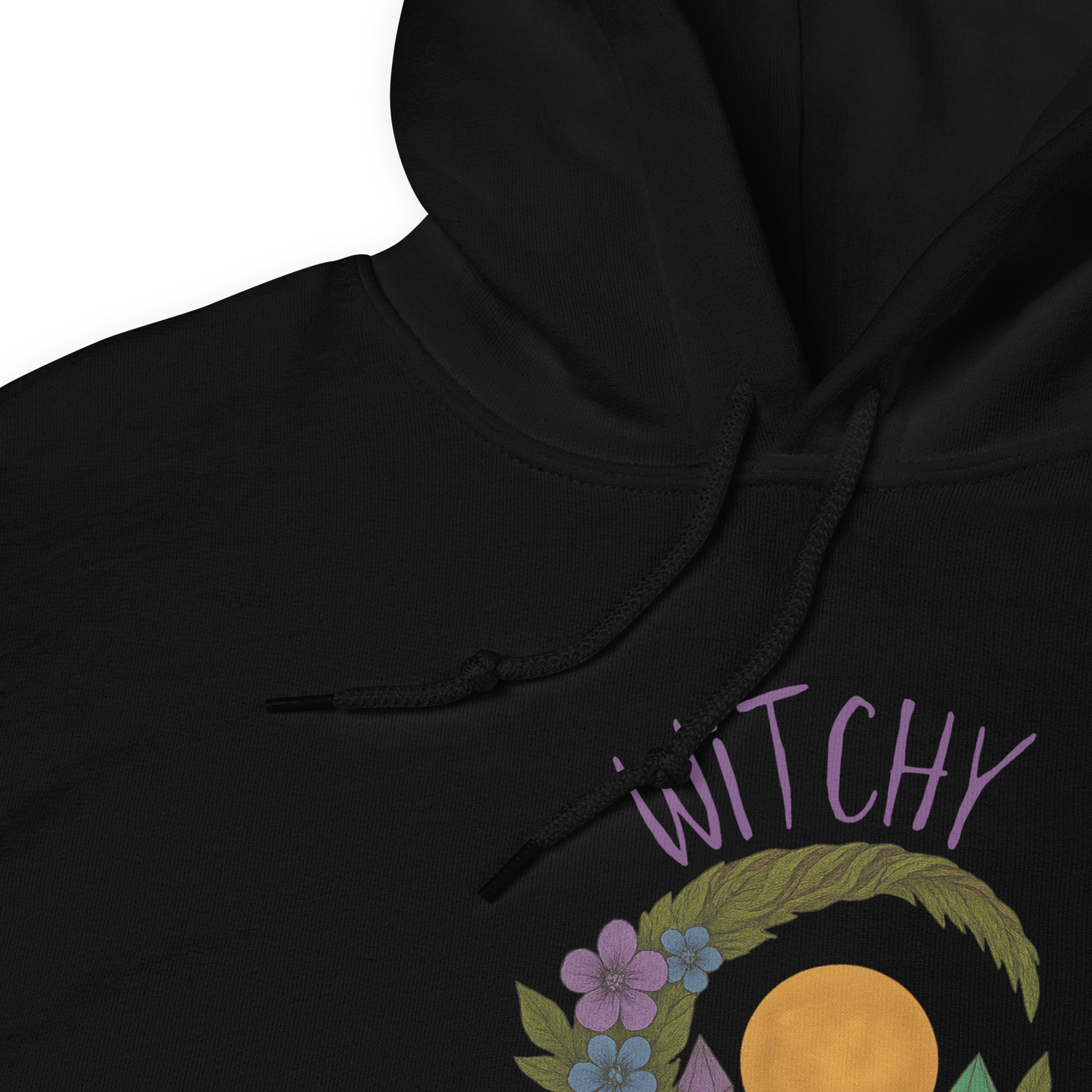 This is a zoom in of a black hoodie with a design of a hand-drawn wreath made of moss-covered branches wraps around a glowing sun. The wreath is decorated with purple and blue flowers, small amethyst and fluorite crystals, and strands of hanging moss. The words “Witchy” curve above the wreath and “All Year” sits on the bottom right