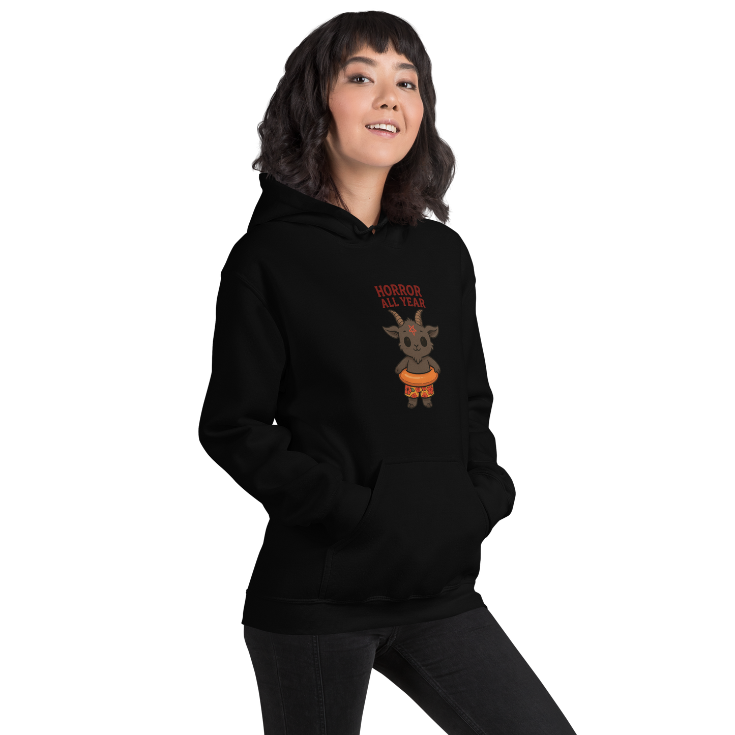 This is a girl with dark hair wearing a black hoodie with a cartoon illustration of a baby Baphomet goat with curved horns and a playful grin, wearing bright floral swim trunks while floating in a colorful inner tube. The character is set against a light background with the bold text “Horror All Year” above in red letters