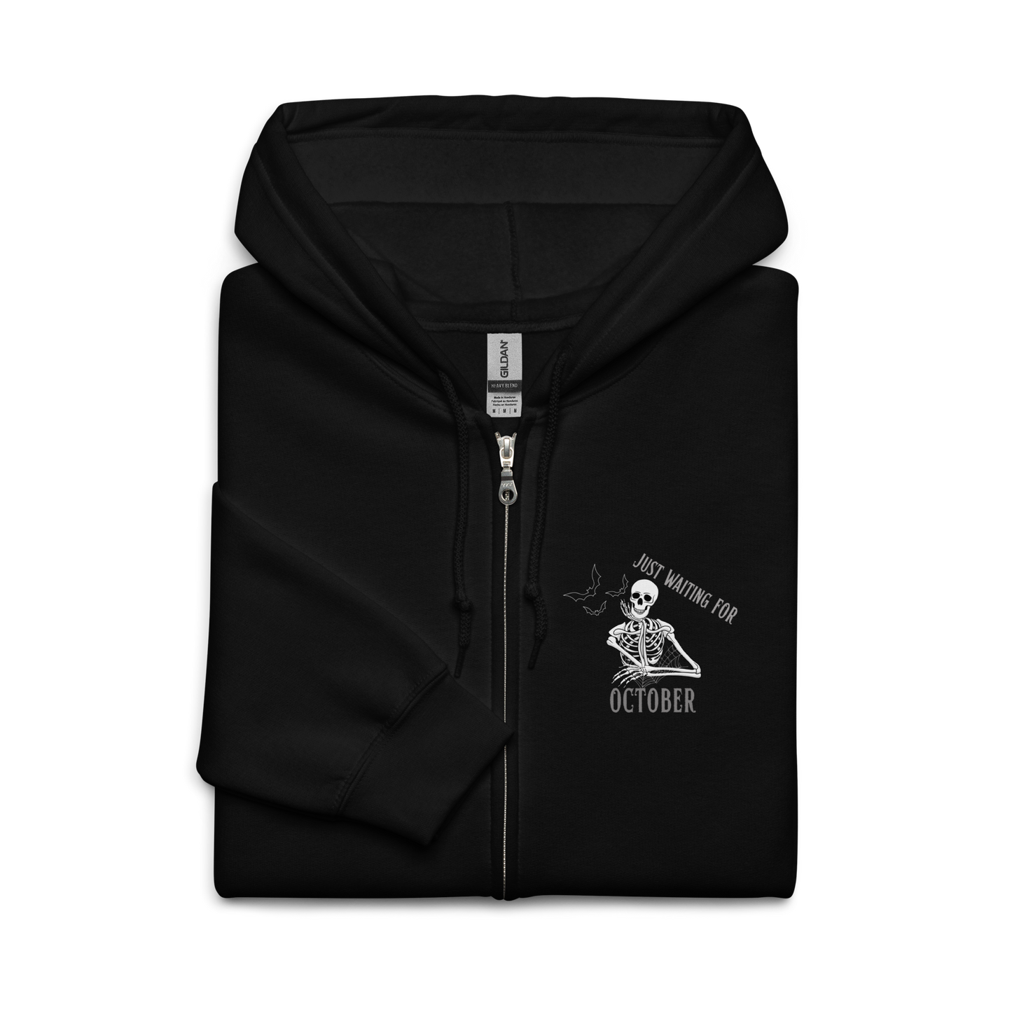 This is a folded black zip-up hoodie that has a bored skeleton with his head resting in his hand and he has spider webs and bats around him and the text reads just waiting for October