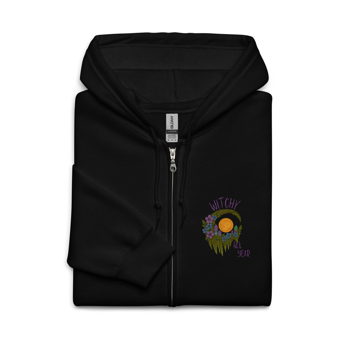 This is a folded black zip-up hoodie with a design of a hand-drawn wreath made of moss-covered branches wraps around a glowing sun. The wreath is decorated with purple and blue flowers, small amethyst and fluorite crystals, and strands of hanging moss. The words “Witchy” curve above the wreath and “All Year” sits on the bottom right
