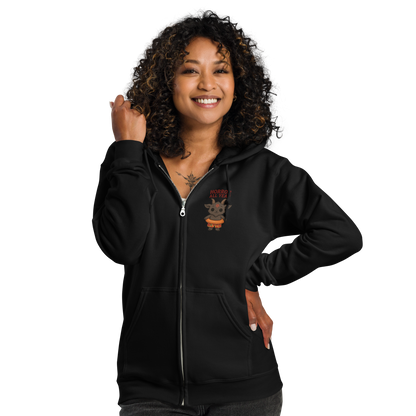This is a woman with dark hair wearing a black zip-up hoodie with a cartoon illustration of a baby Baphomet goat with curved horns and a playful grin, wearing bright floral swim trunks while floating in a colorful inner tube. The character is set against a light background with the bold text “Horror All Year” above in red letters