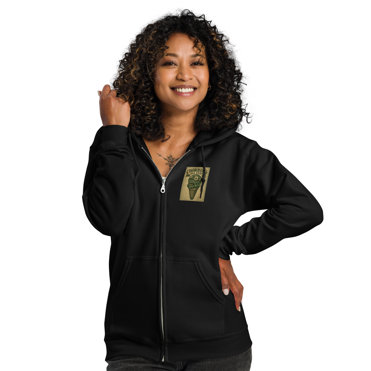 This is a woman with dark curly hair wearing a black zip-up hoodie that is a vintage-style illustration of a zombie-themed ice cream cone with a green, melting undead face and bulging eyeballs. Above the cone, a horror banner reads "Horror All Year" on a distressed parchment background