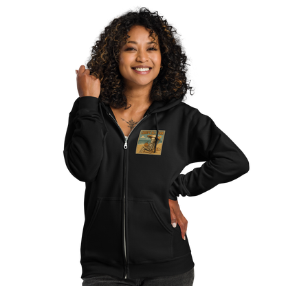 This is a woman with black curly hair wearing a black zip-up hoodie with a retro-style illustration of a grinning skeleton lounging on a beach chair under an orange umbrella. The skeleton is holding a pumpkin-shaped drink cup with a straw and relaxing by the ocean, with a bright sun in the sky and a life preserver in the sand. The words “Creepy All Year” appear boldly at the top
