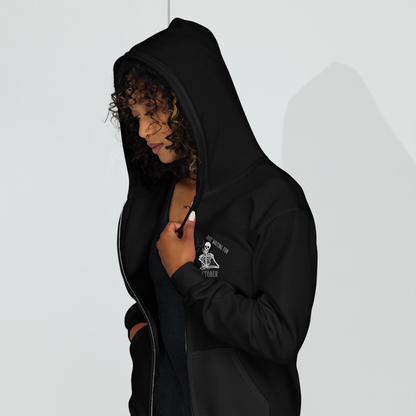 This is a woman with dark curly hair wearing a black zip-up hoodie that has a bored skeleton with his head resting in his hand and he has spider webs and bats around him and the text reads just waiting for October