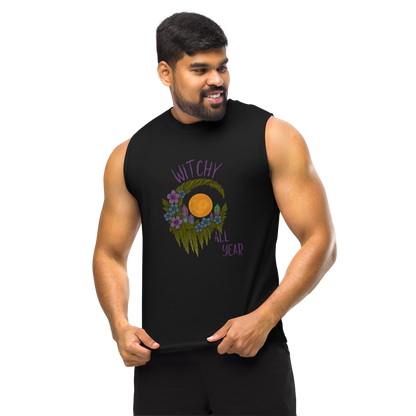 This is a man with dark hair wearing a black muscle shirt with a design of a hand-drawn wreath made of moss-covered branches wraps around a glowing sun. The wreath is decorated with purple and blue flowers, small amethyst and fluorite crystals, and strands of hanging moss. The words “Witchy” curve above the wreath and “All Year” sits on the bottom right 
