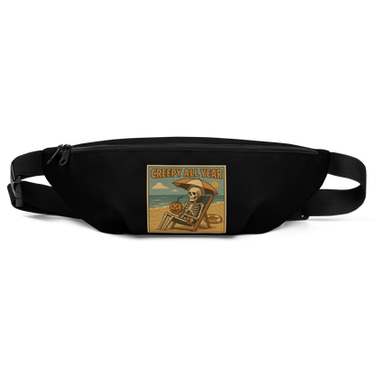 This is a black waist bag fanny pack with a retro-style illustration of a grinning skeleton lounging on a beach chair under an orange umbrella. The skeleton is holding a pumpkin-shaped drink cup with a straw and relaxing by the ocean, with a bright sun in the sky and a life preserver in the sand. The words “Creepy All Year” appear boldly at the top 