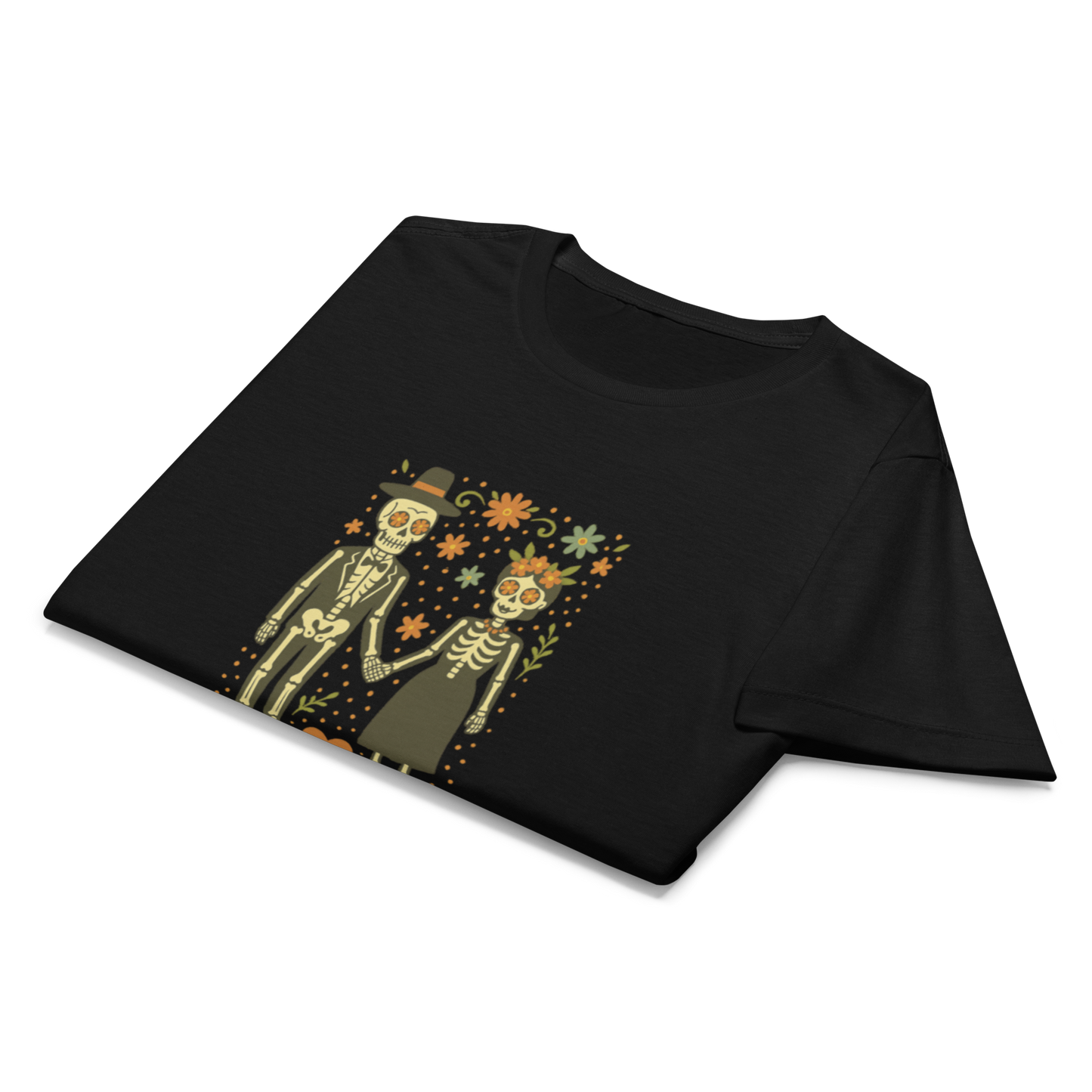 This is a folded black women's t-shirt with a Día de los Muertos–style illustration of a male and female skeleton holding hands, surrounded by marigolds, vines, and folk art patterns. The skeletons wear traditional black clothing, the man in a suit and hat, the woman with a floral crown with a red heart and leaves at the bottom and the text Creepy All Year. Rendered in warm tones of orange, green, and cream, symbolizing eternal love and remembrance