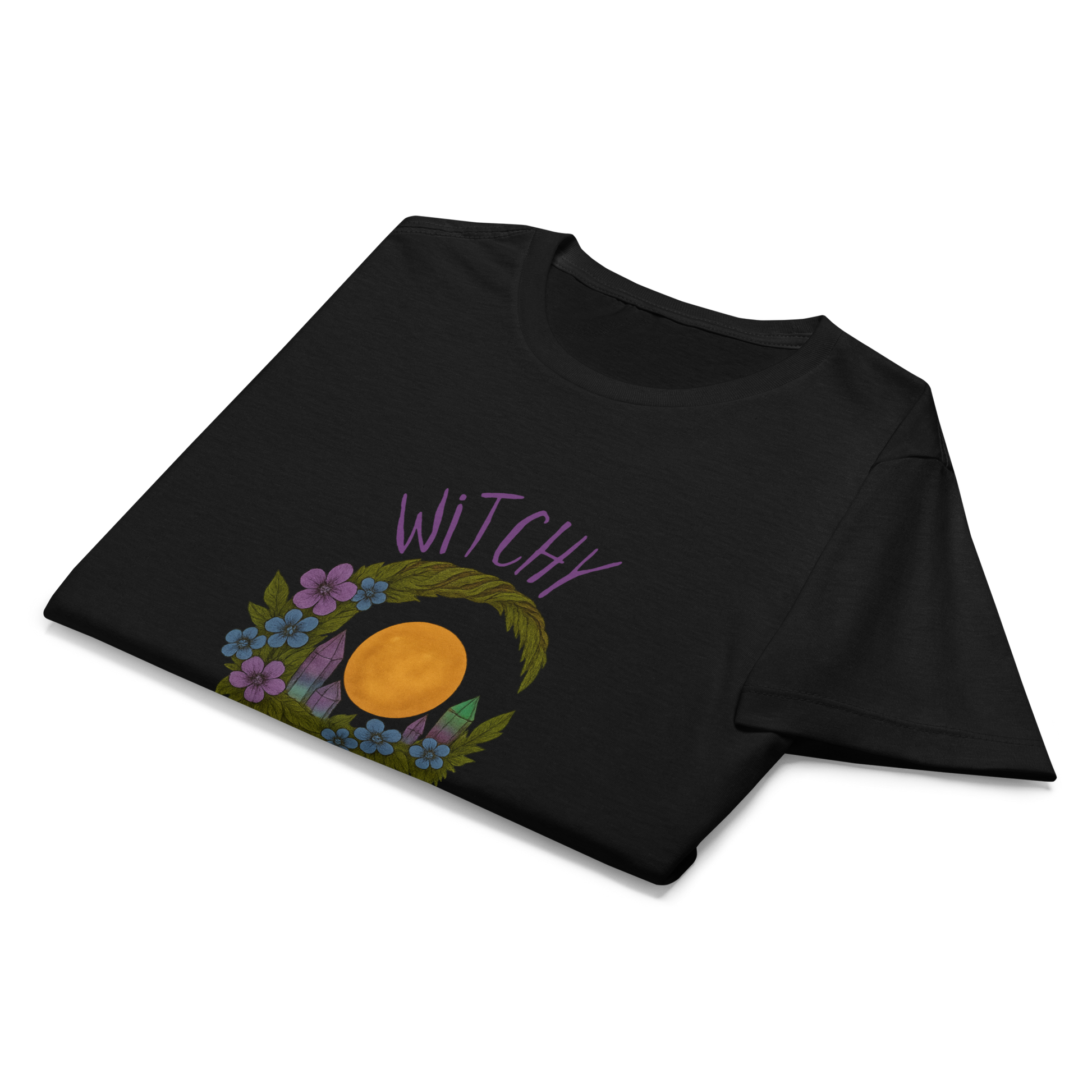 This is a folded black women's t-shirt with a design of a hand-drawn wreath made of moss-covered branches wraps around a glowing sun. The wreath is decorated with purple and blue flowers, small amethyst and fluorite crystals, and strands of hanging moss. The words “Witchy” curve above the wreath and “All Year” sits on the bottom right 
