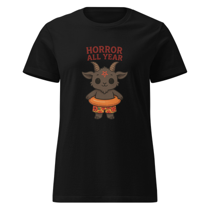 This is a women's black t-shirt with a cartoon illustration of a baby Baphomet goat with curved horns and a playful grin, wearing bright floral swim trunks while floating in a colorful inner tube. The character is set against a light background with the bold text “Horror All Year” above in red letters