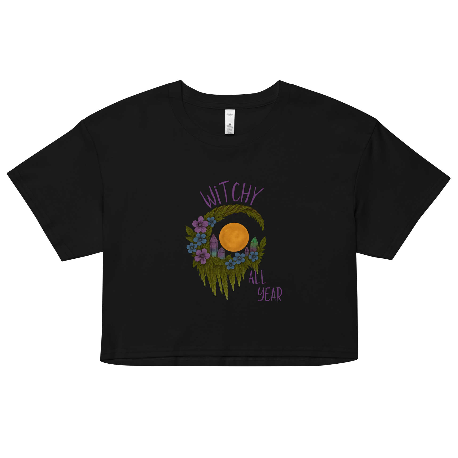 This is a black crop top with a design of a hand-drawn wreath made of moss-covered branches wraps around a glowing sun. The wreath is decorated with purple and blue flowers, small amethyst and fluorite crystals, and strands of hanging moss. The words “Witchy” curve above the wreath and “All Year” sits on the bottom right 
