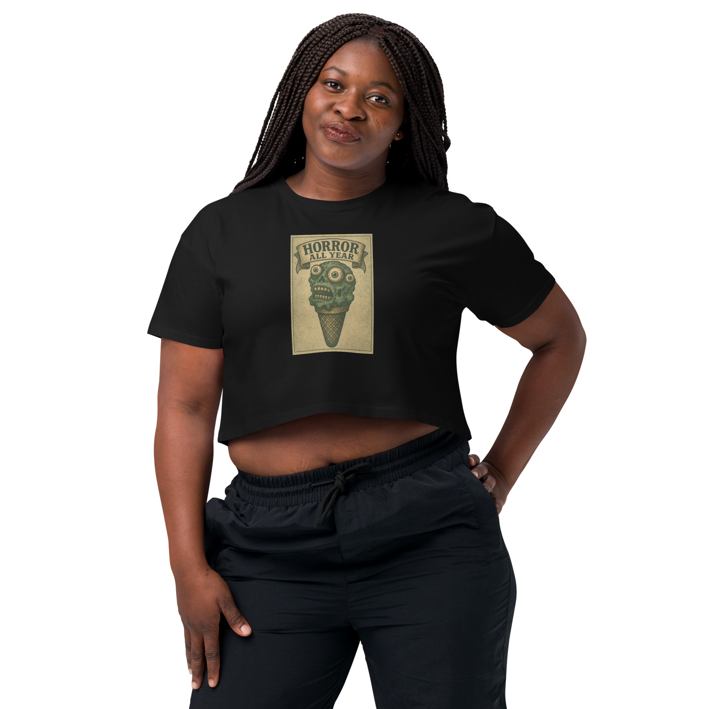 This is a woman with dark braids wearing a black crop top that is a vintage-style illustration of a zombie-themed ice cream cone with a green, melting undead face and bulging eyeballs. Above the cone, a horror banner reads "Horror All Year" on a distressed parchment background