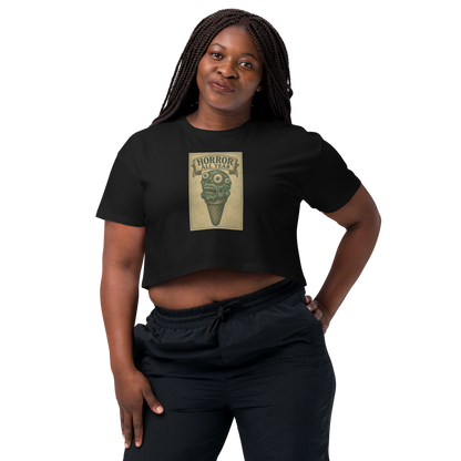 This is a woman with dark braids wearing a black crop top that is a vintage-style illustration of a zombie-themed ice cream cone with a green, melting undead face and bulging eyeballs. Above the cone, a horror banner reads "Horror All Year" on a distressed parchment background