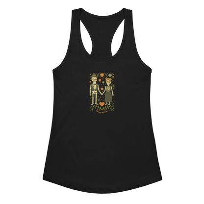 This is a black women's racerback tank top with a Día de los Muertos–style illustration of a male and female skeleton holding hands, surrounded by marigolds, vines, and folk art patterns. The skeletons wear traditional black clothing, the man in a suit and hat, the woman with a floral crown with a red heart and leaves at the bottom and the text Creepy All Year. Rendered in warm tones of orange, green, and cream, symbolizing eternal love and remembrance