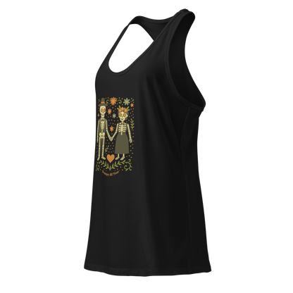 This is a black women's racerback tank top with a Día de los Muertos–style illustration of a male and female skeleton holding hands, surrounded by marigolds, vines, and folk art patterns. The skeletons wear traditional black clothing, the man in a suit and hat, the woman with a floral crown with a red heart and leaves at the bottom and the text Creepy All Year. Rendered in warm tones of orange, green, and cream, symbolizing eternal love and remembrance
