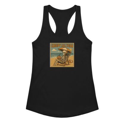 This is a black racerback tank top with a retro-style illustration of a grinning skeleton lounging on a beach chair under an orange umbrella. The skeleton is holding a pumpkin-shaped drink cup with a straw and relaxing by the ocean, with a bright sun in the sky and a life preserver in the sand. The words “Creepy All Year” appear boldly at the top 